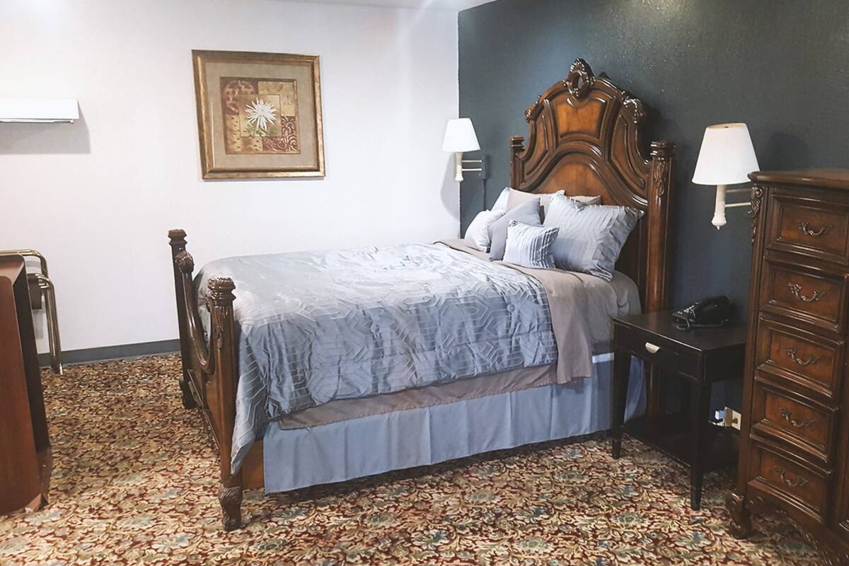 Ein Schlafzimmer mit einem hölzernen Bett, einem gemusterten Teppich, einem Schminktisch und einer Wandlampe.