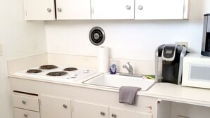 Een keuken met een kookplaat, spoelbak, magnetron en kastjes.