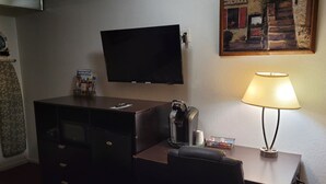 Een hotelkamer met een flatscreen televisie aan de muur, een bureau met een lamp, een koffiezetapparaat en een stoel.