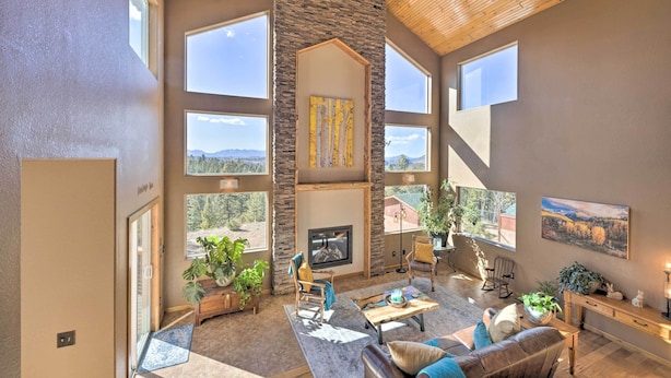 A spacious living room with a stone fireplace, large windows, and a high ceiling. - Woodland Park Home w/ Mountain Views By ATV Trails (Woodland Park)
