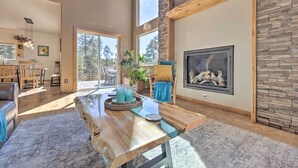 A spacious living room with a large wooden dining table, a fireplace, and a stone accent wall. - Woodland Park Home w/ Mountain Views By ATV Trails (Woodland Park)