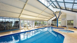 An indoor swimming pool with clear glass walls, a covered roof, and sun loungers. - Broadwater Beach Villa | Pool, Spa & Tennis (Broadwater)