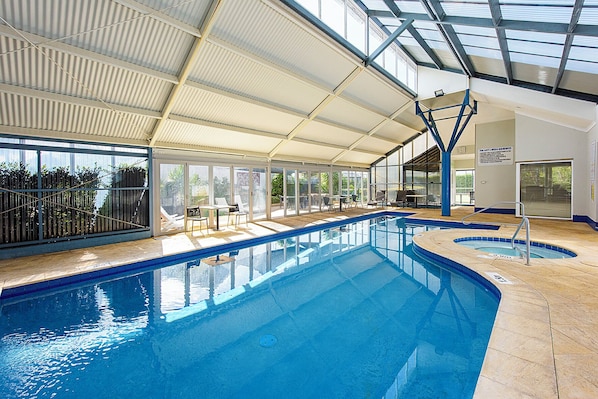 An indoor swimming pool with clear glass walls, a covered roof, and sun loungers. - Broadwater Beach Villa | Pool, Spa & Tennis (Broadwater)