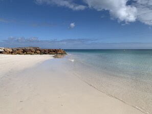 A beach with clear water, a rocky breakwater, and a sandy shore.