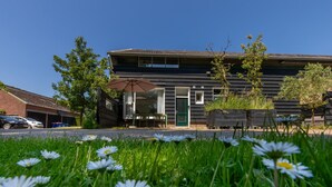 A modern building with a flat roof, a covered outdoor seating area, and a parking lot. - 4-Person Stay at Rustenpolder (Vrouwenpolder)