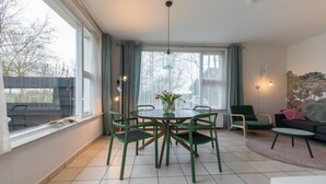 A modern living room with a round table and chairs, a sofa, a coffee table, and a view of trees through large windows. - 4-Person Stay at Rustenpolder (Vrouwenpolder)