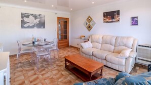A living room with a beige sofa, a wooden coffee table, and a glass dining table with chairs. - Le Giono by Interhome (Saint Laurent du Var)