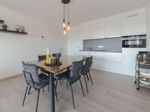 A modern kitchen with white cabinets, a stainless steel oven, and a dining area with a wooden table and four chairs.