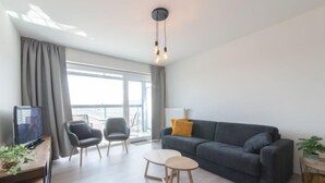 Una sala moderna con un sofá gris, dos sillones, una mesita redonda y un televisor sobre un mueble de madera.