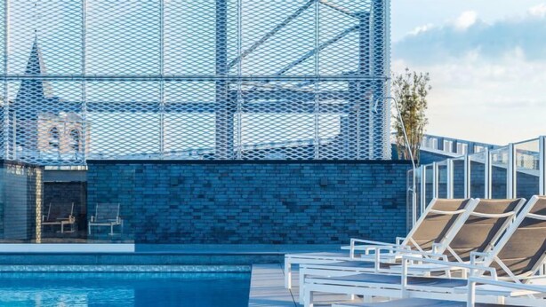 Zona de piscina en la azotea con sillones de descanso y vistas a un edificio con fachada de celosía.