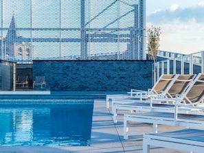 A rooftop pool area with lounge chairs and a view of a building with a lattice facade.