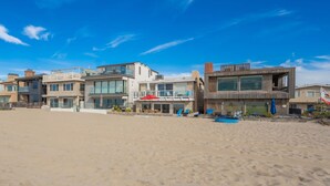 Een strandhuis met moderne architectuur, inclusief een zwembadgedeelte met ligbedden en parasols.