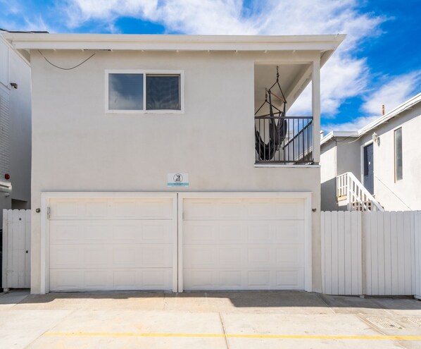 A two-story house with a white exterior, a small balcony with a metal railing, and a garage with two white doors.