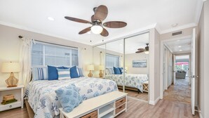 Un dormitorio con una cama grande, ventilador de techo, un espejo y vista al exterior.