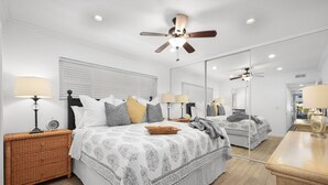 A modern bedroom with a large bed, two bedside tables with lamps, a ceiling fan, and a large mirror. - Spacious 3 Bedroom Home w/ Fire Pit at the Beach! (Newport Beach)