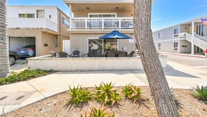 A two-story building with a balcony, outdoor seating area, and a parking garage. - Spacious 3 Bedroom Home w/ Fire Pit at the Beach! (Newport Beach)