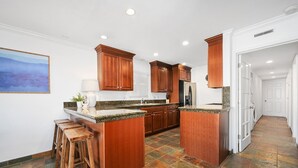 A modern kitchen with wooden cabinets, granite countertops, and a central island. - Spacious 3 Bedroom Home w/ Fire Pit at the Beach! (Newport Beach)