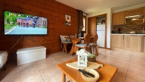A cozy living room with a wooden TV wall, a dining area with wooden chairs, and a kitchen with wooden cabinets. - Quiet apartment in Samoëns with pool and WiFi (Samoëns)