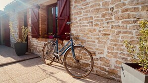 Ein Gebäude aus Stein mit einer gefliesten Terrasse, einem Fahrrad und Topfpflanzen.