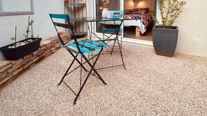 Eine Terrasse mit zwei blauen Stühlen und einem Tisch, einem Blumentopf und einem kleinen Blumenbeet mit Pflanzen.