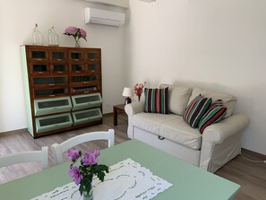 Ein Wohnzimmer mit einem Holzschrank, einem beigen Sofa, einem Tisch mit einer Spitzenleinentischdecke und einem Sessel.