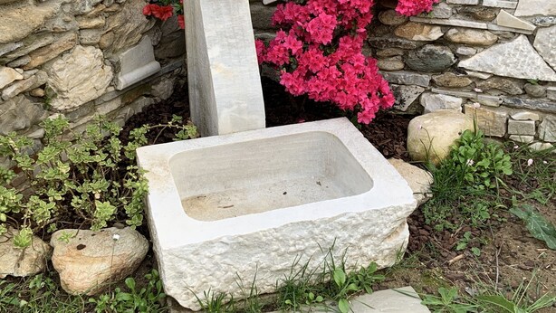 Un vaso in pietra con un bacino rettangolare, un muro in pietra e fiori rosa.