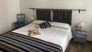 Un letto ben rifatto con copripiumino a righe e cuscini, un comodino con una lampada, e una sedia.