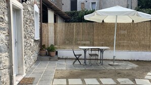 Un patio con tavolo e sedie, un ombrellone bianco e un gatto.
