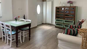 Zona pranzo con tavolo e sedie in legno, un mobile con ante in vetro e un divano con cuscini a righe.