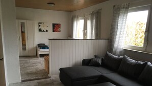 A living room with a dark sofa, a small table, and a view of a kitchen and dining area through an open door.