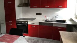 A compact kitchen with red cabinets, a stove, and a sink.