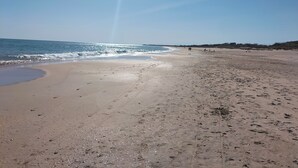 En bred sandstrand med fotspår och en klar himmel.