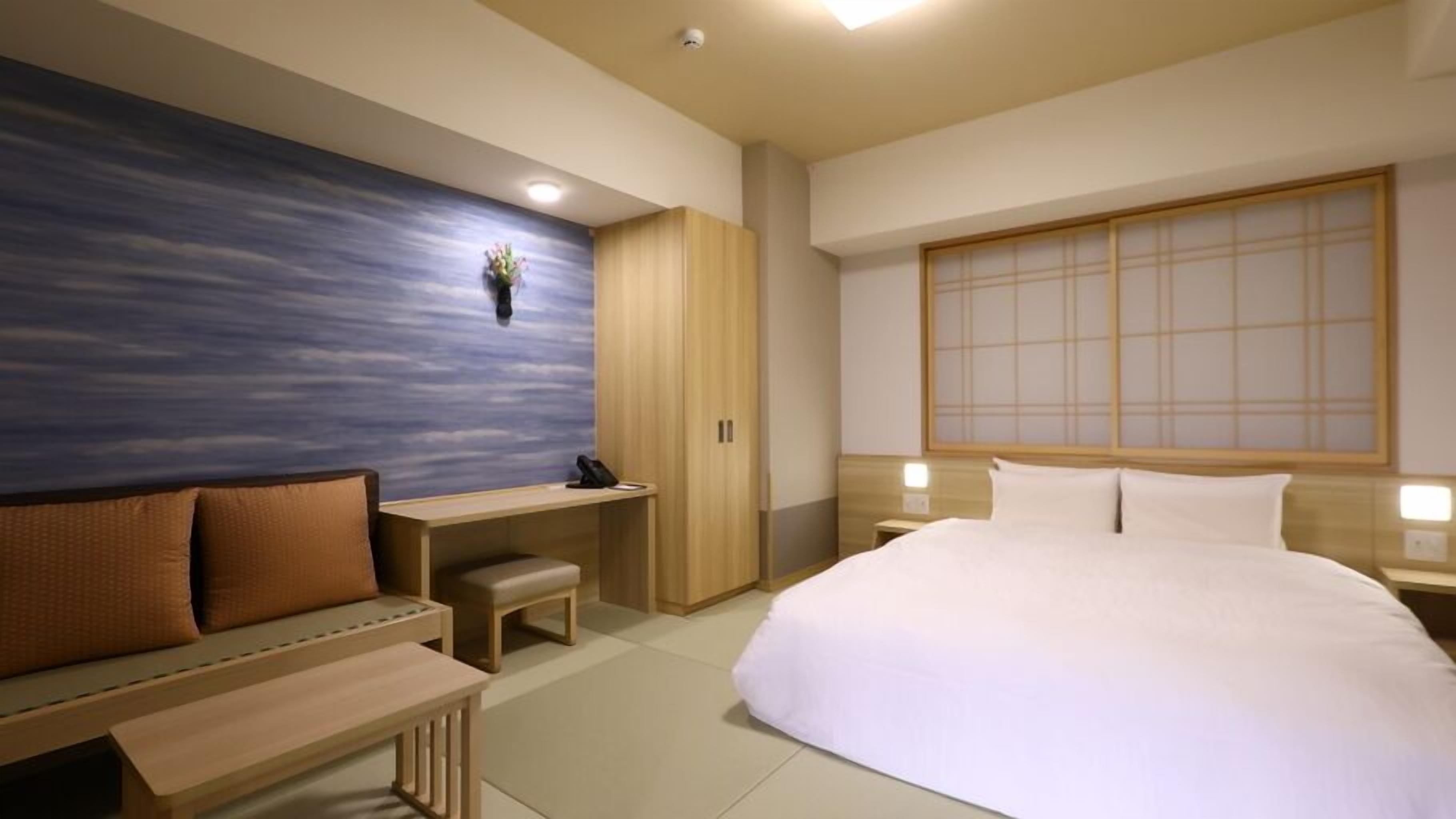 Una habitación de hotel moderna con cama, escritorio, banca y armario.