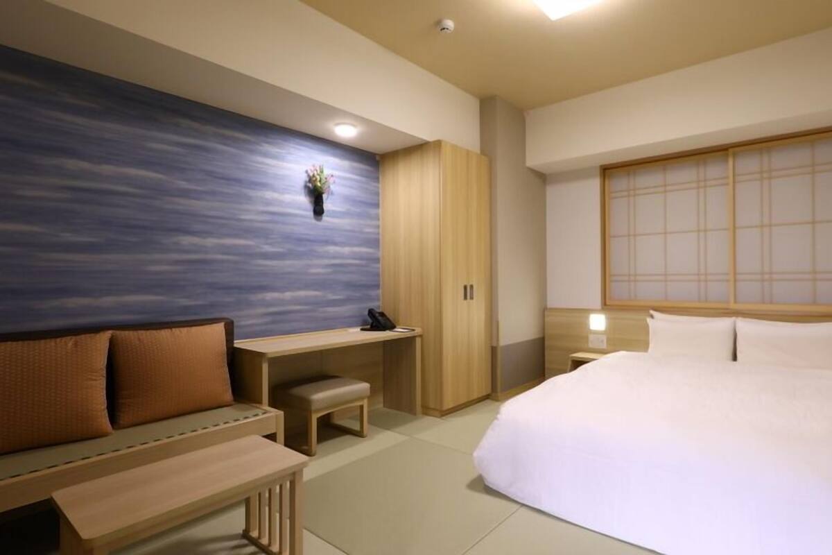 A modern hotel room with a bed, a desk, a bench, and a wardrobe.