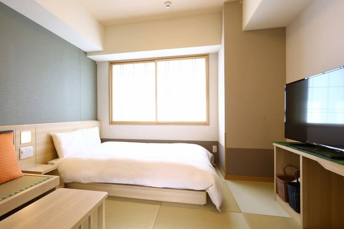 A hotel room with a bed, a TV, a desk, and a window.
