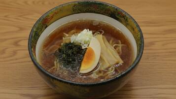 A bowl of ramen soup with noodles, a soft-boiled egg, and seaweed garnish on a wooden table.
