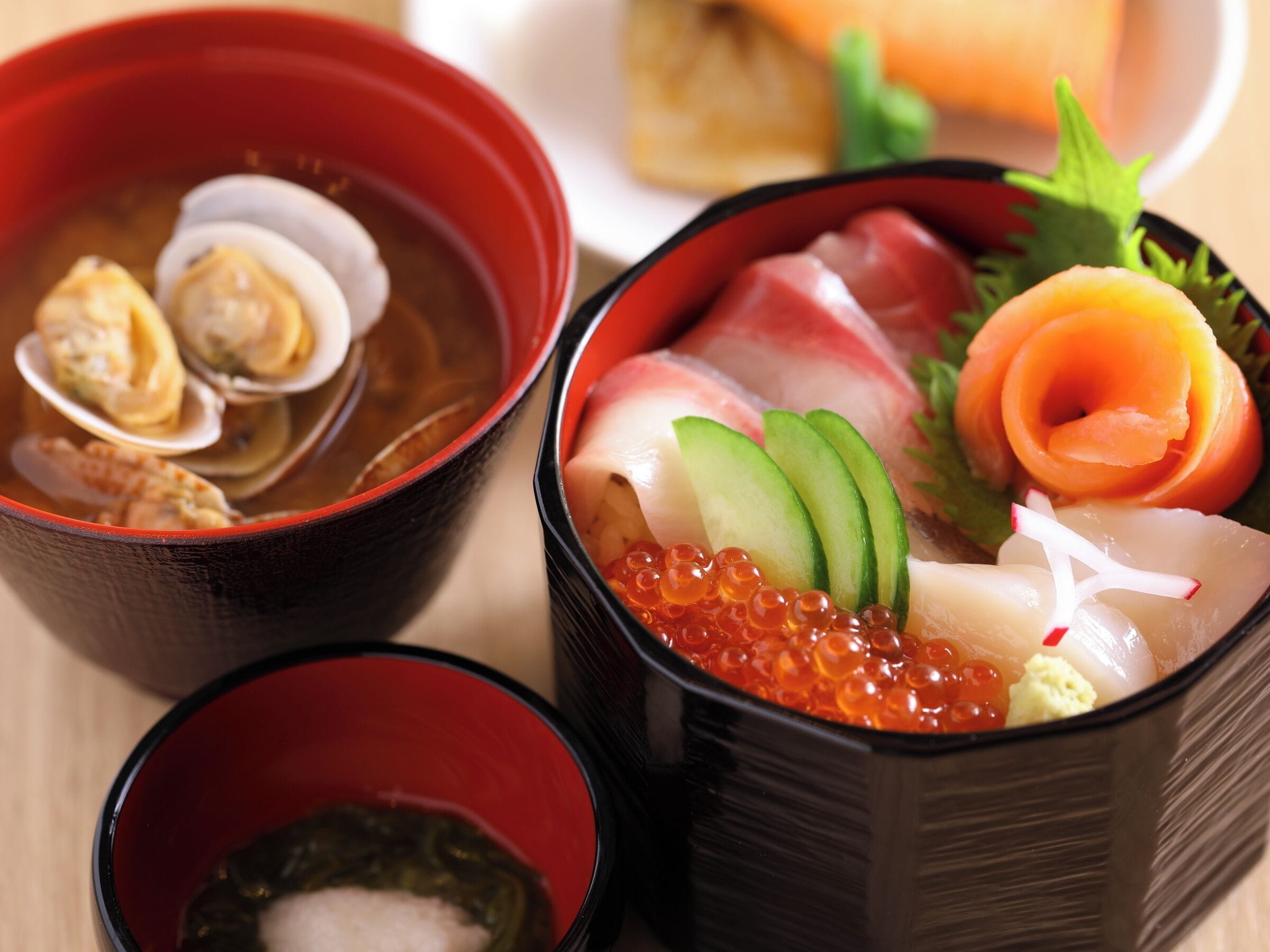 A traditional Japanese meal with sashimi, salmon, and roe, served in black bowls.