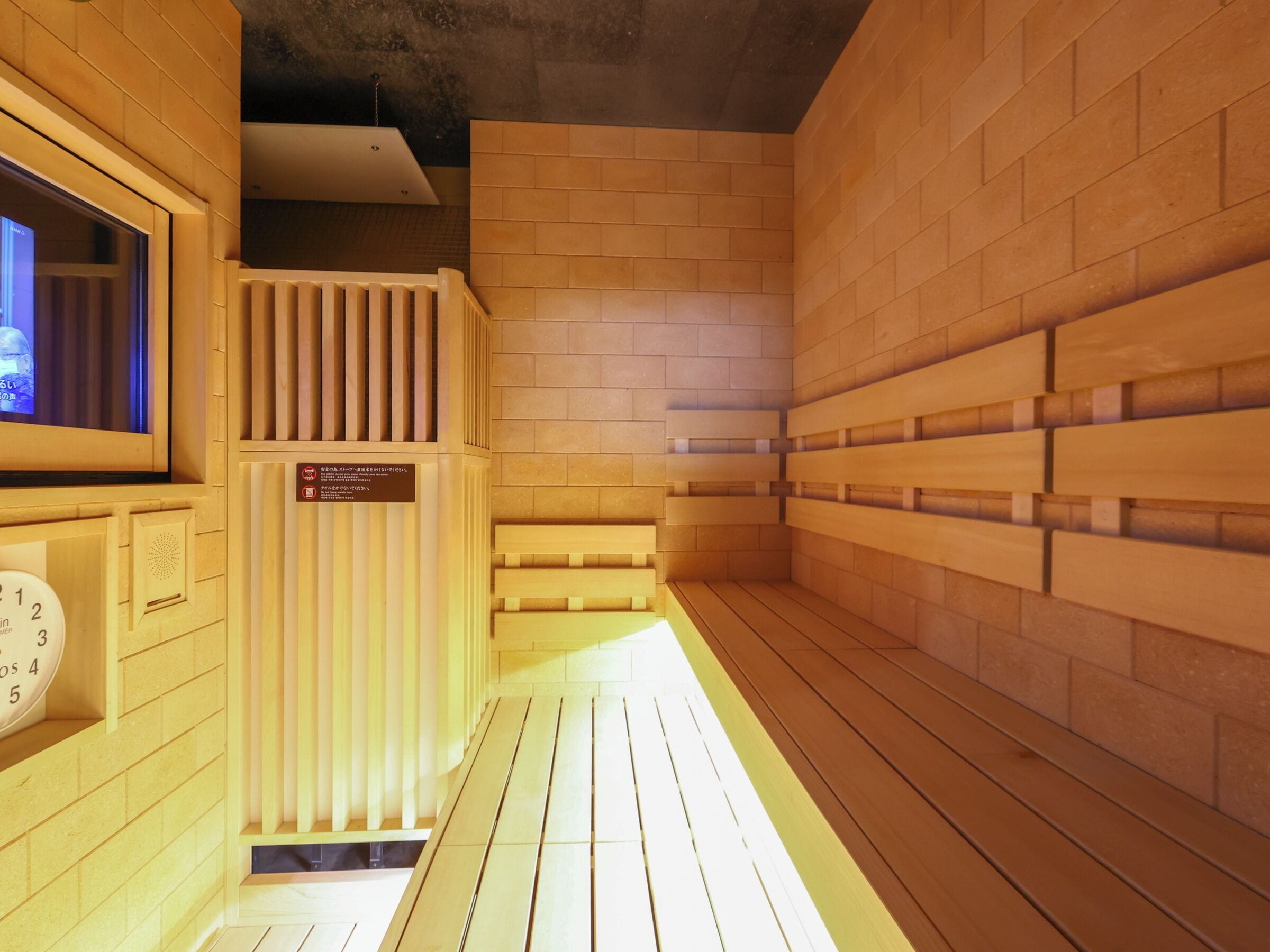 Un sauna avec des bancs en bois, une horloge et un écran de télévision.