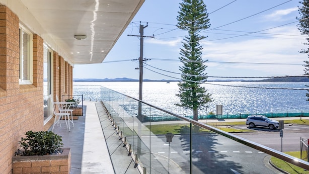 A balcony with a view of a body of water, a road with a car, and a clear sky.
