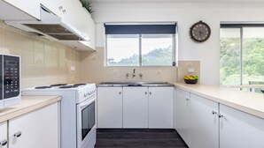 A modern kitchen with white cabinets, a stove, and a window with a view of greenery.