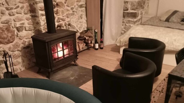 A cozy room with a stone wall, a wooden heater, a bed, and a hot tub. - Stationery discs, ideal for lovers! (Saint-Laurent-le-Minier)