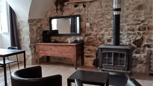 A cozy room with a stone wall, a wooden dresser, a mirror, a fireplace, and a table with chairs. - Stationery discs, ideal for lovers! (Saint-Laurent-le-Minier)
