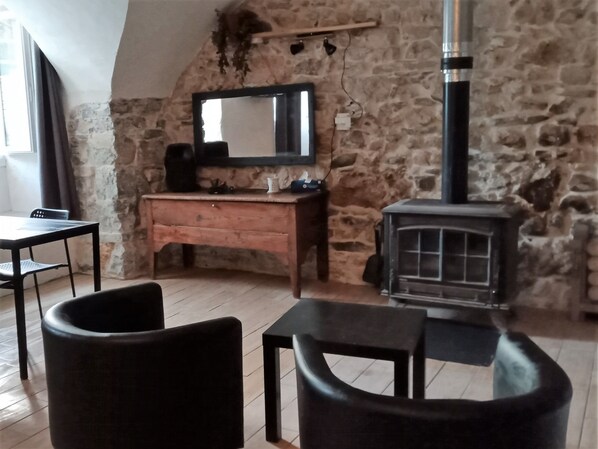 A cozy room with a stone wall, a wooden dresser, a mirror, a fireplace, and a table with chairs.