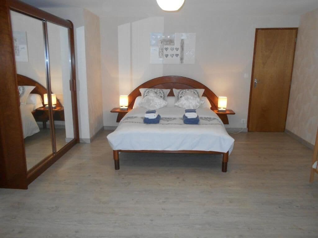 A bedroom with a wooden bed, two bedside tables with lamps, a large mirror, and a door.