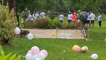 A group of people in a garden with a dirt path, surrounded by greenery and balloons.