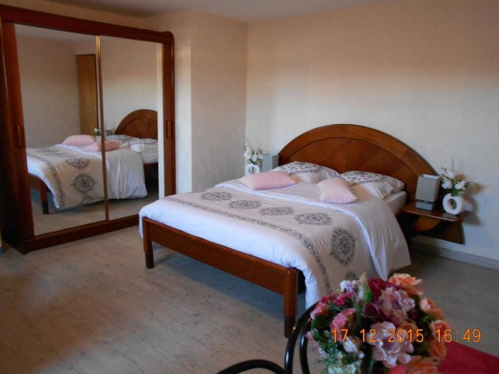 A bedroom with a wooden bed, a mirror, and a nightstand with a lamp.
