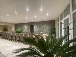 A modern conference room with a long table, multiple chairs, a stone wall, and ceiling lights.