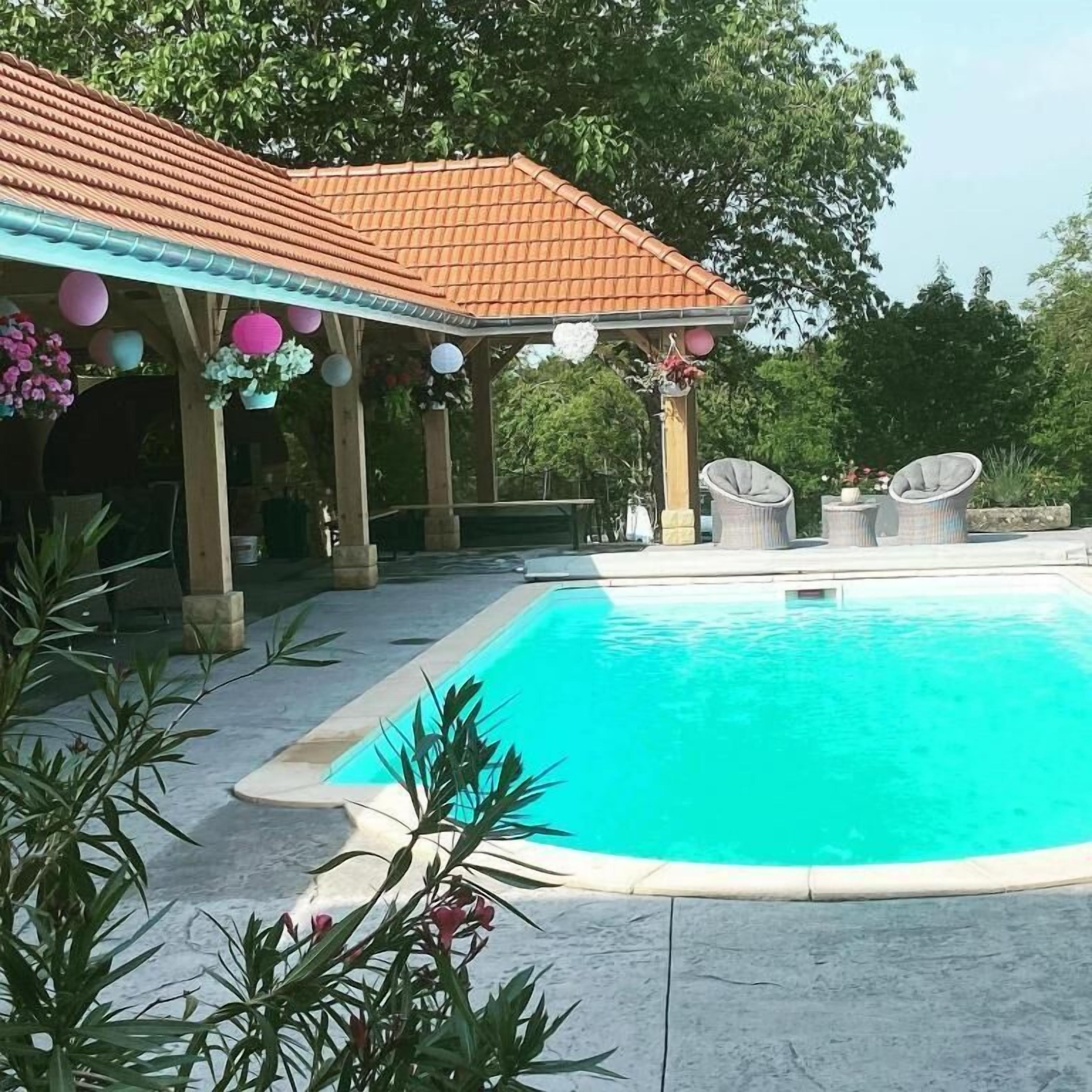 Una piscina con borde de baldosas, rodeada de plantas en macetas y mobiliario de exterior.