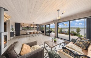 A modern interior with a kitchen, dining area, and a large sliding glass door leading to a deck with a lake view. - 4 bedroom nice home in Sannidal (Sannidal)