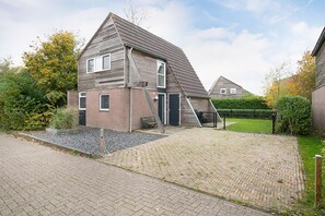 A two-story house with a sloped roof, a paved driveway, and a small garden area with a bench and a wooden fence. - Beautiful vacation home on watery recreation park Yn'e Lijte Grou  (Grou)